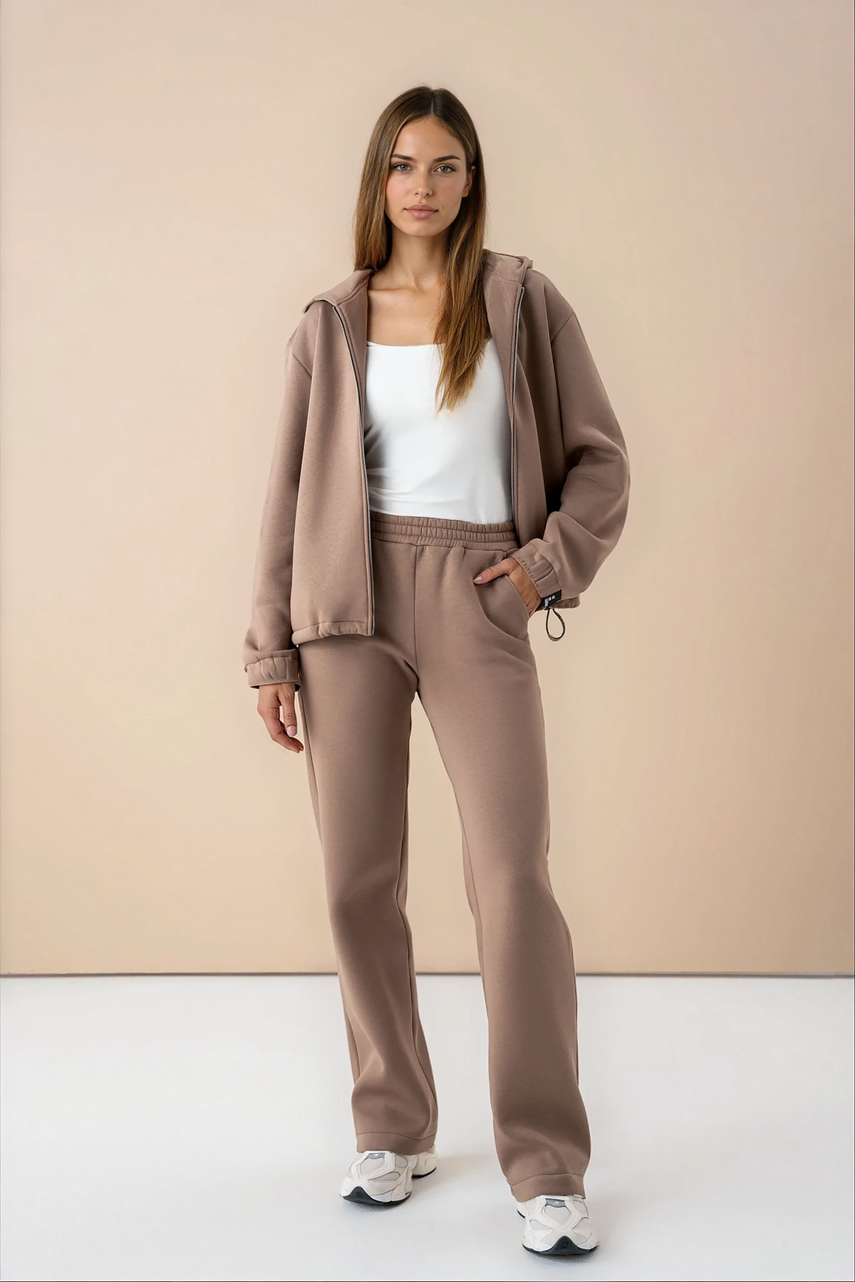 woman wearing latte-colored cutmyfashion tracksuit with a zipper, in a studio setting, with a white top underneath