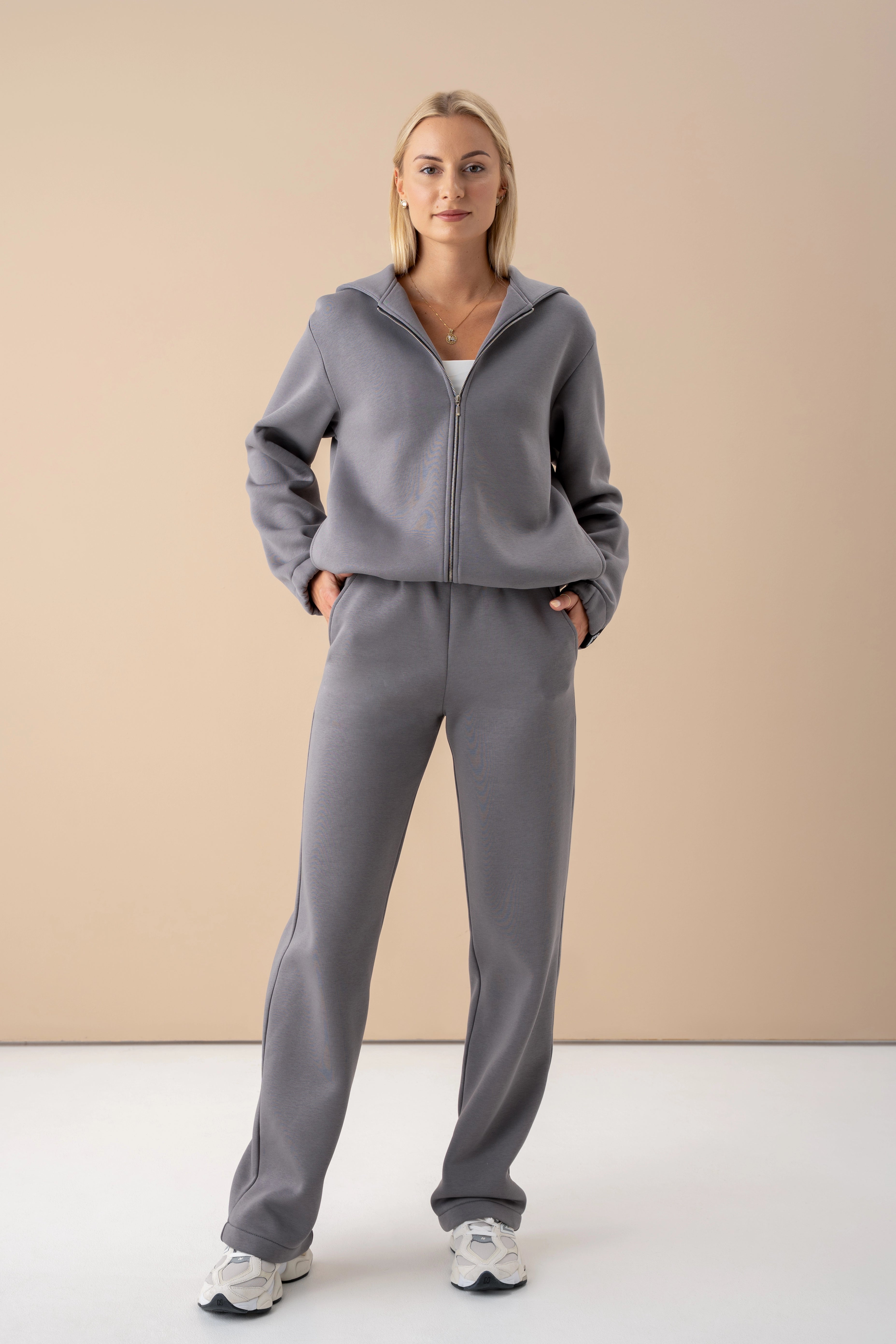 modelis dėvi pilką laisvalaikio kostiumą su užtraukiamu džemperiu, rankas įkišusi į kišenes, pagaminta Lietuvoje