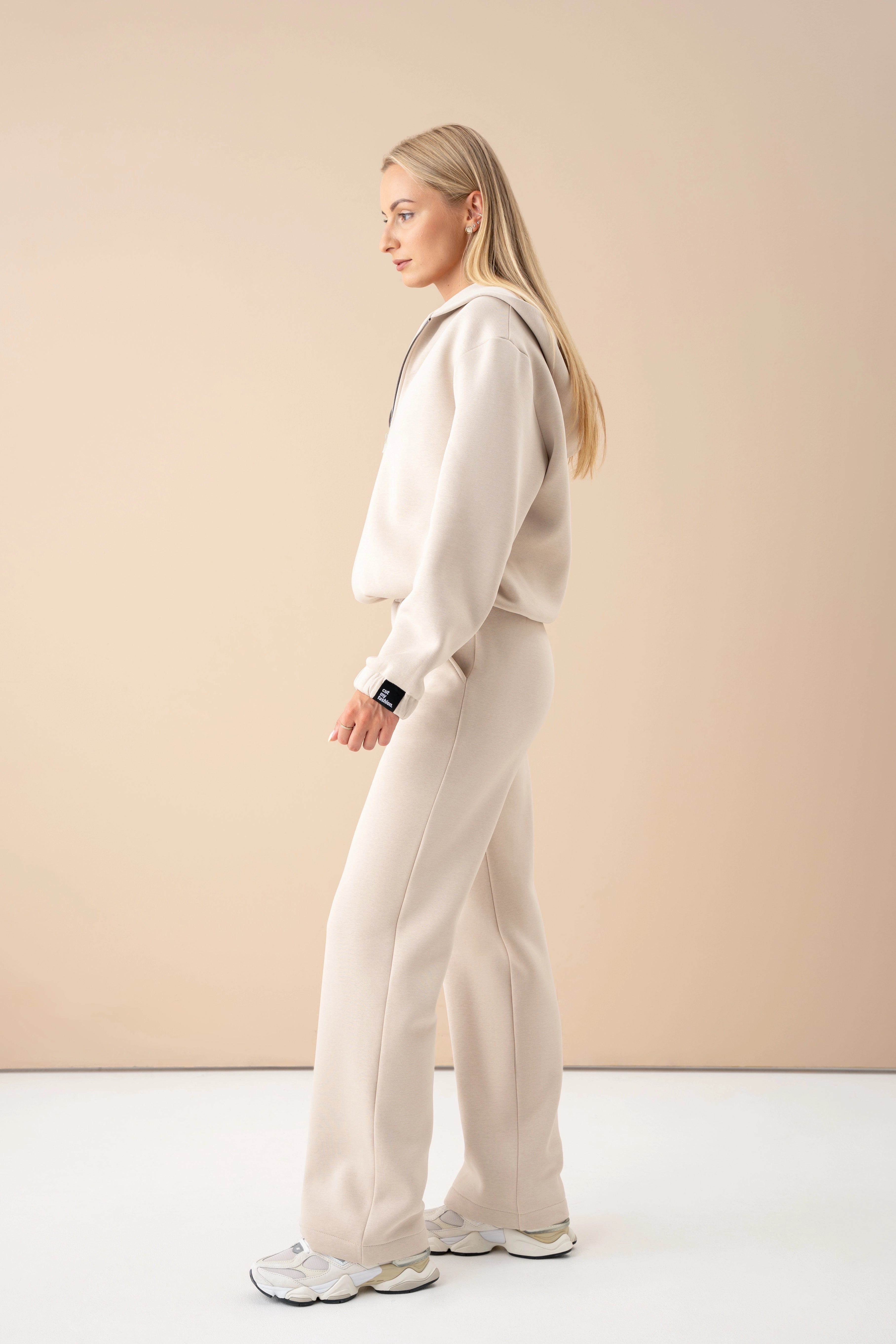 A woman is wearing an oversized sweatshirt and trousers, walking in a studio setting, side view