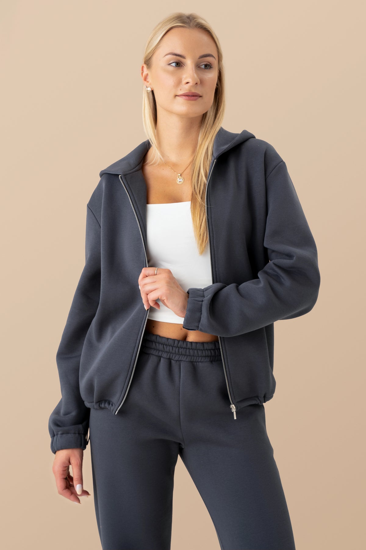 the model is wearing a dark grey cutmyfashion sweatshirt and a white blouse, standing against a light studio background