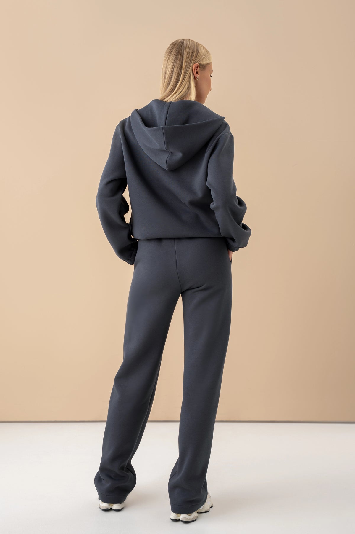 the woman is wearing an iron-colour sweatshirt and trousers, with her back turned to the camera, wearing white trainers