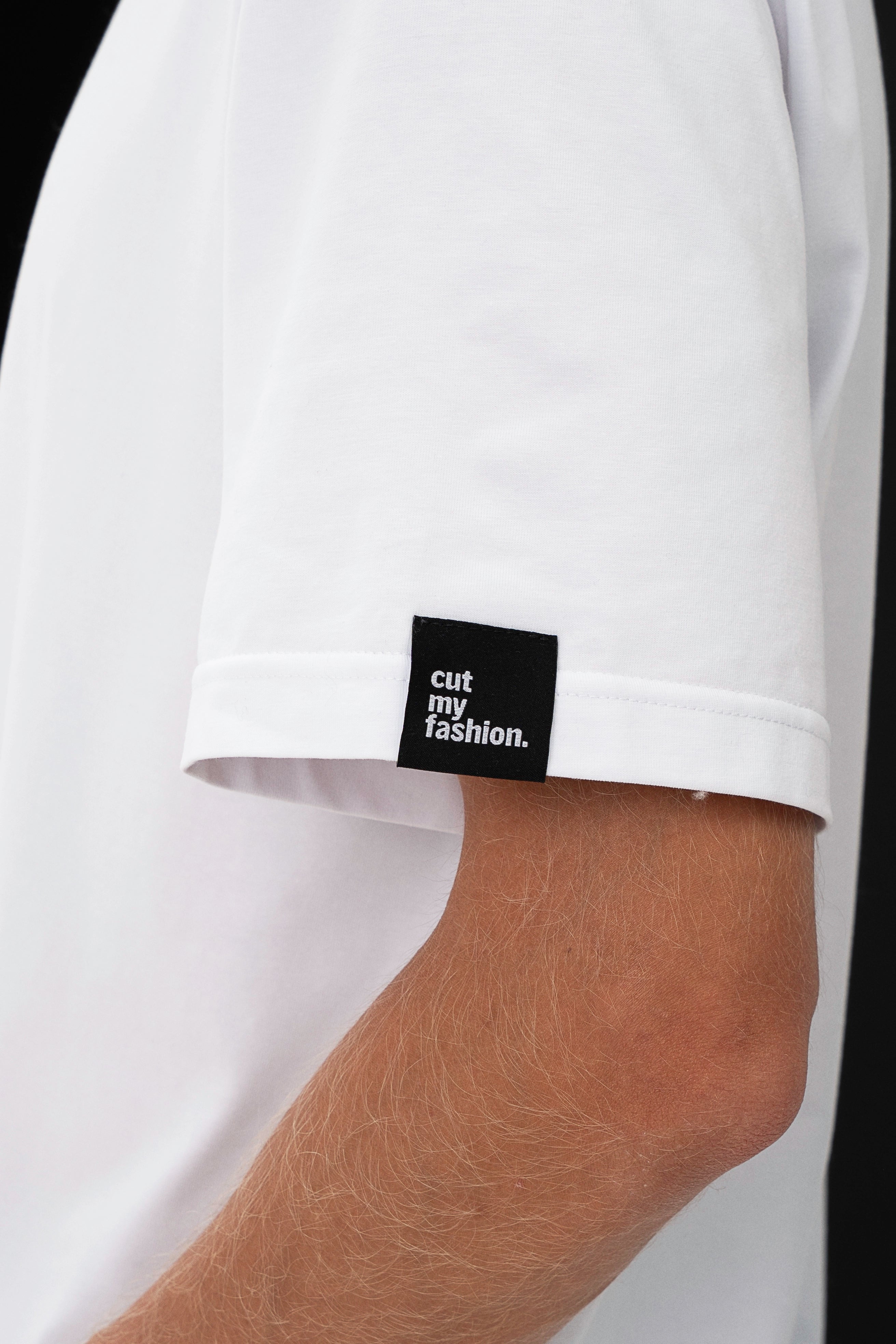 Vyras iš šono pozuoja su baltais marškinėliais, matomas ir juodas prekinio ženklo logotipas cut my fashion ant rankovės