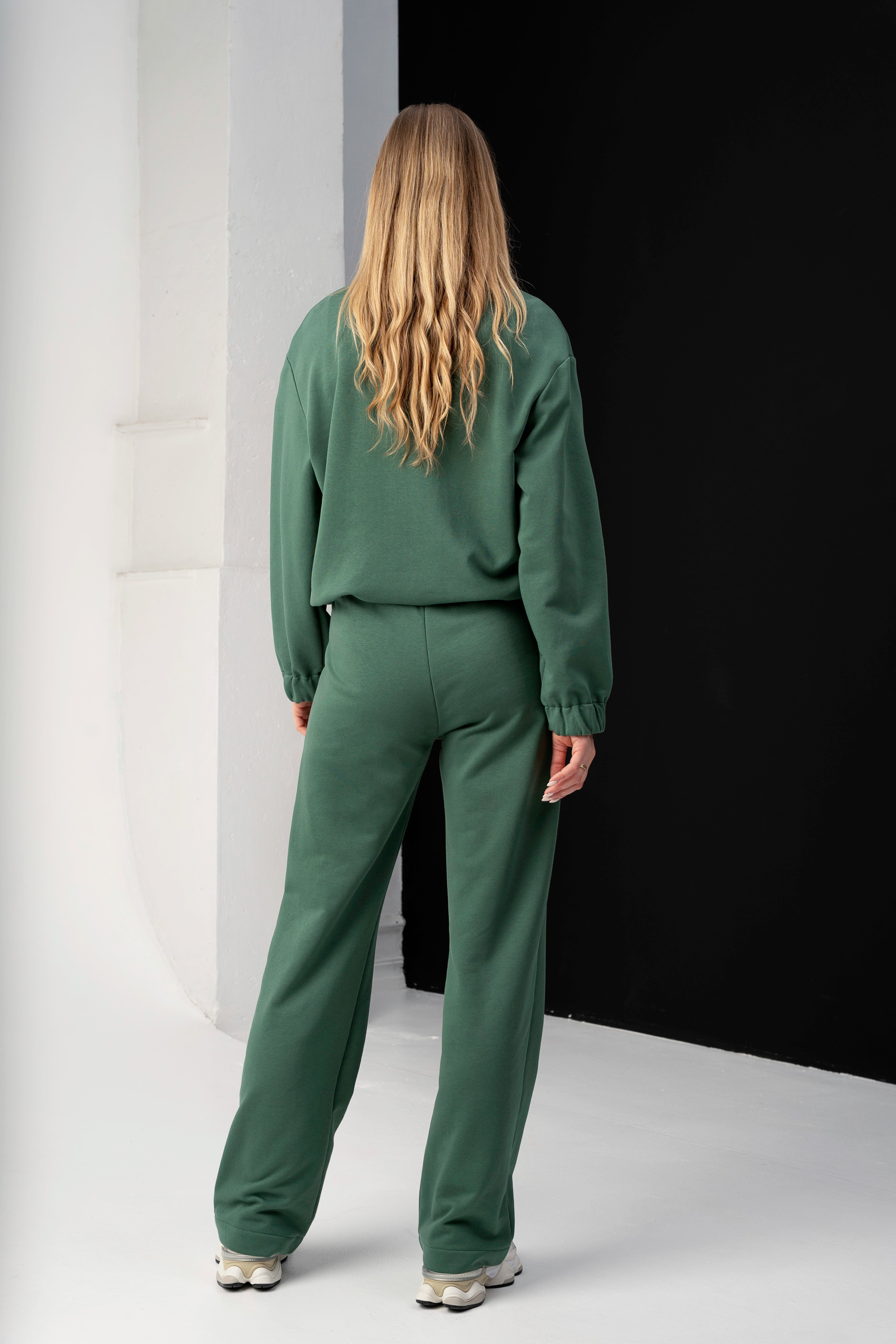 moteris su žaliais cutmyfashion treningais mėja, pozuoja iš nugaros studijos aplinkoje