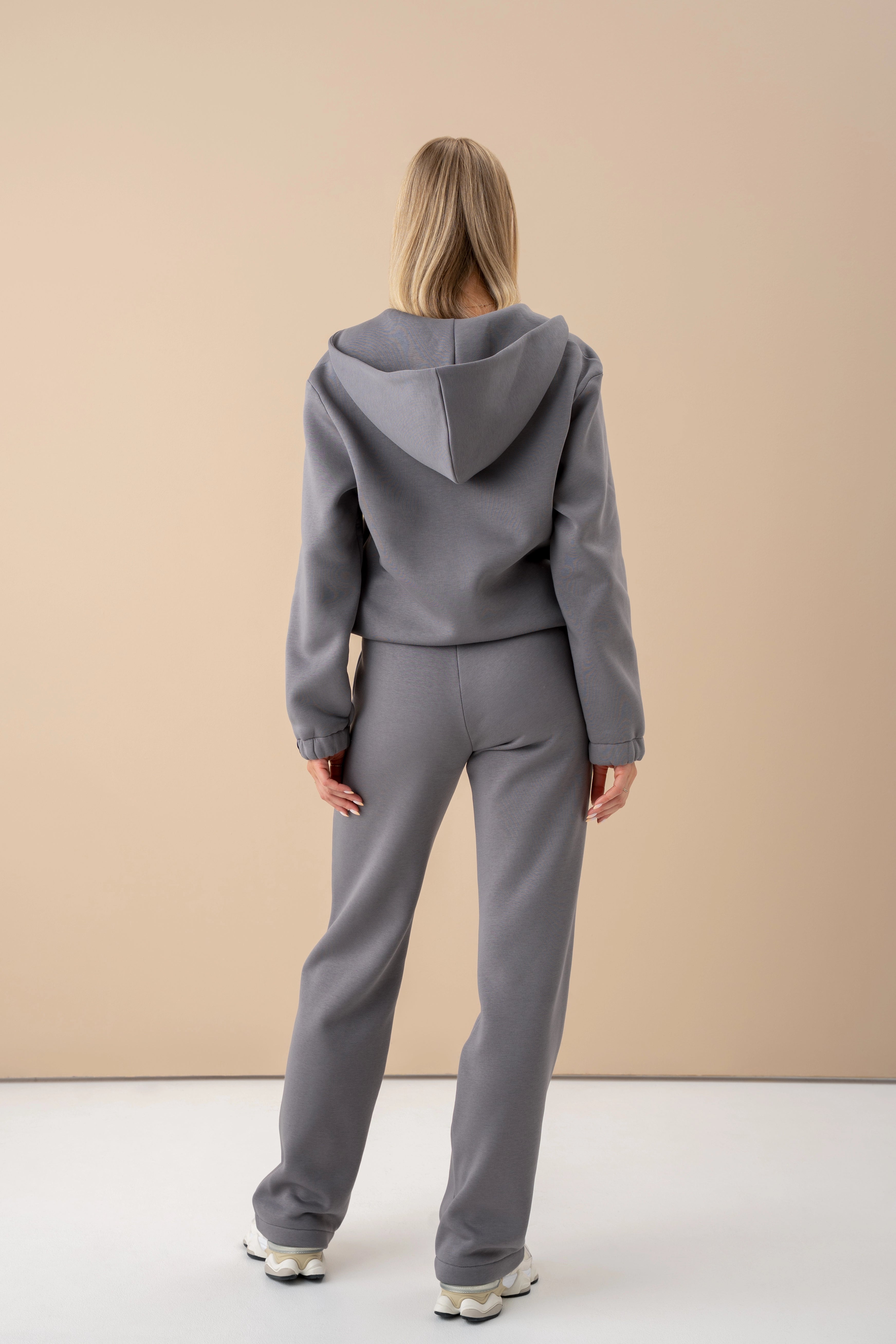 pilkos spalvos treningų komplektas cutmyfashion, modelis stovi nugara į kamerą, dėvi baltus sportinius batelius