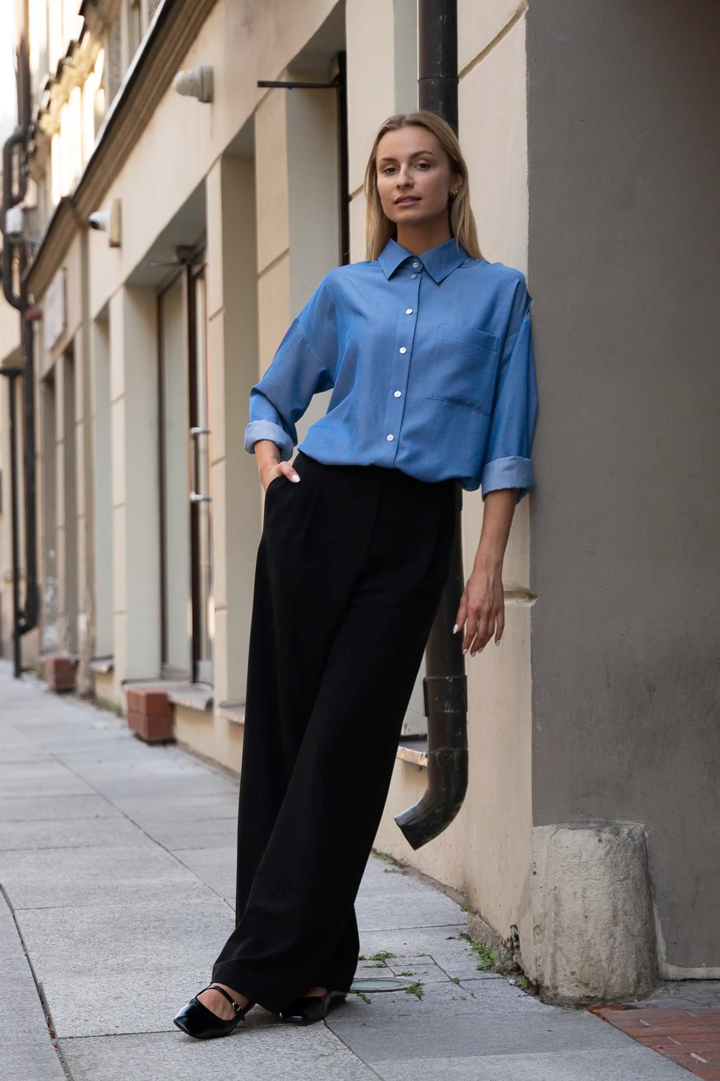 Classic women’s outfit with a blue shirt and black wide-leg trousers, full view on a city street
