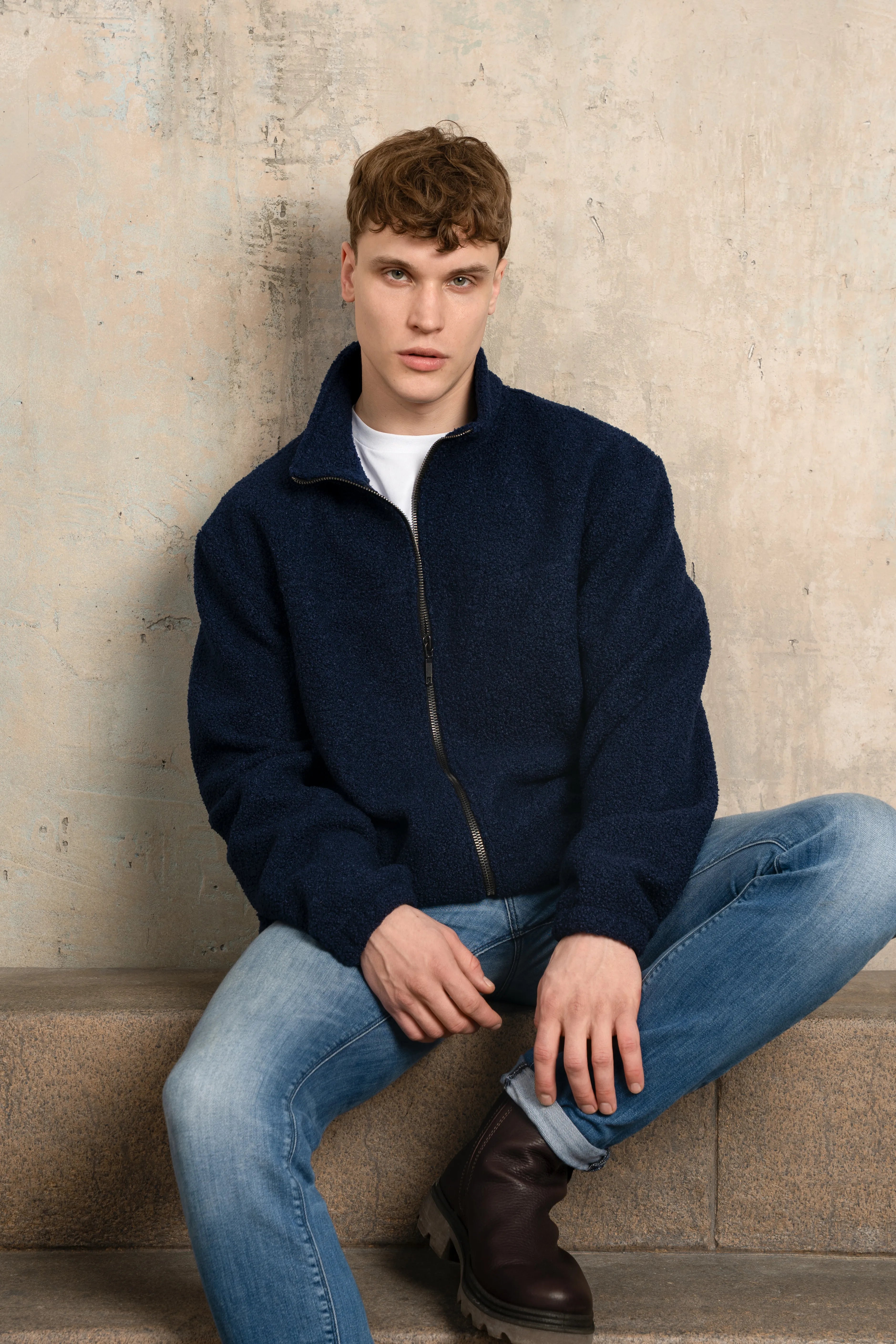 Dark navy men’s zip-up sweatshirt with a full-length zipper, stand-up collar, long sleeves, and a relaxed fit, model photographed seated