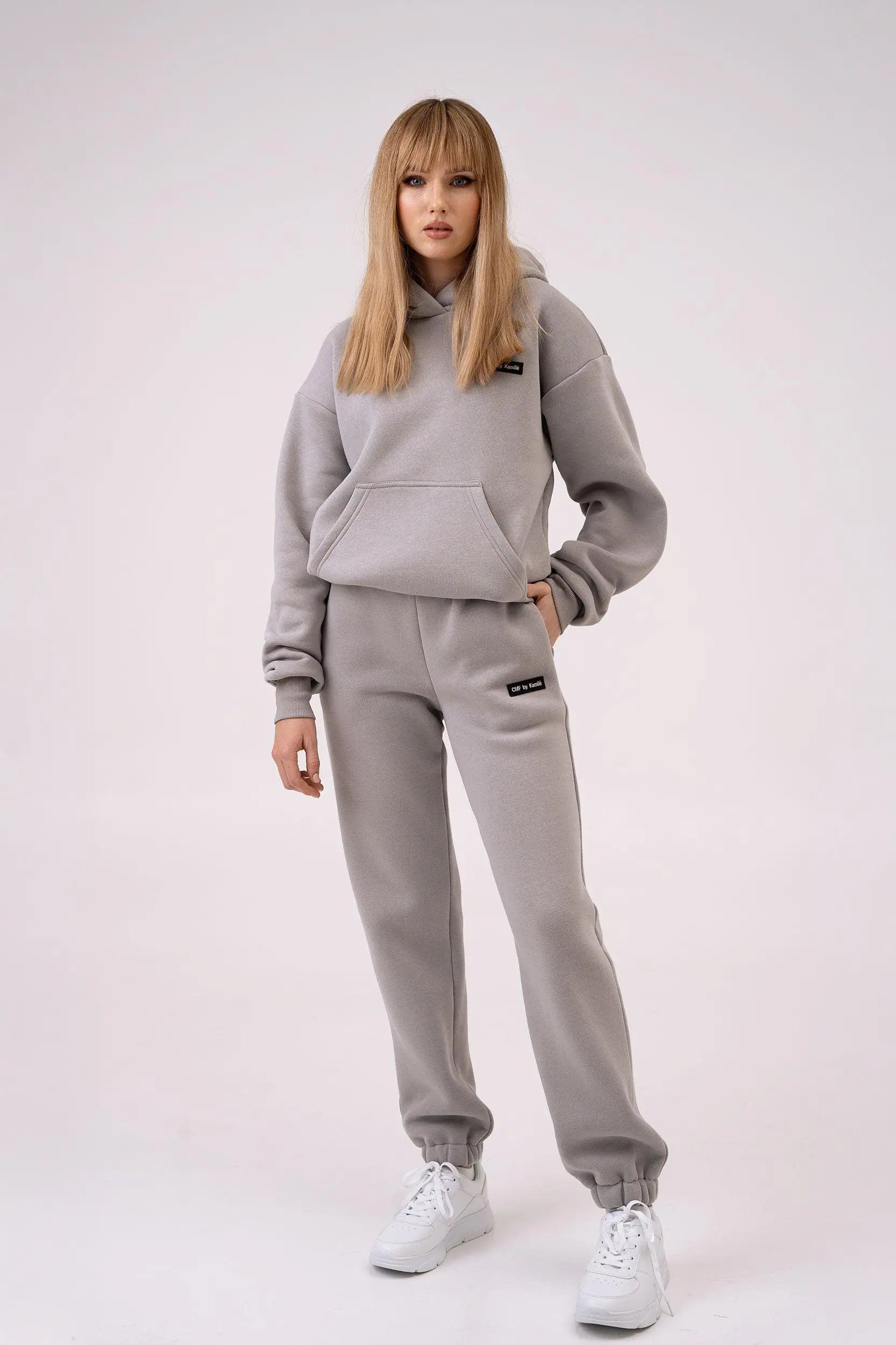 The woman is wearing a cutmyfashion leisure tracksuit, standing against a white background, with one hand in her pocket and the other by her side.