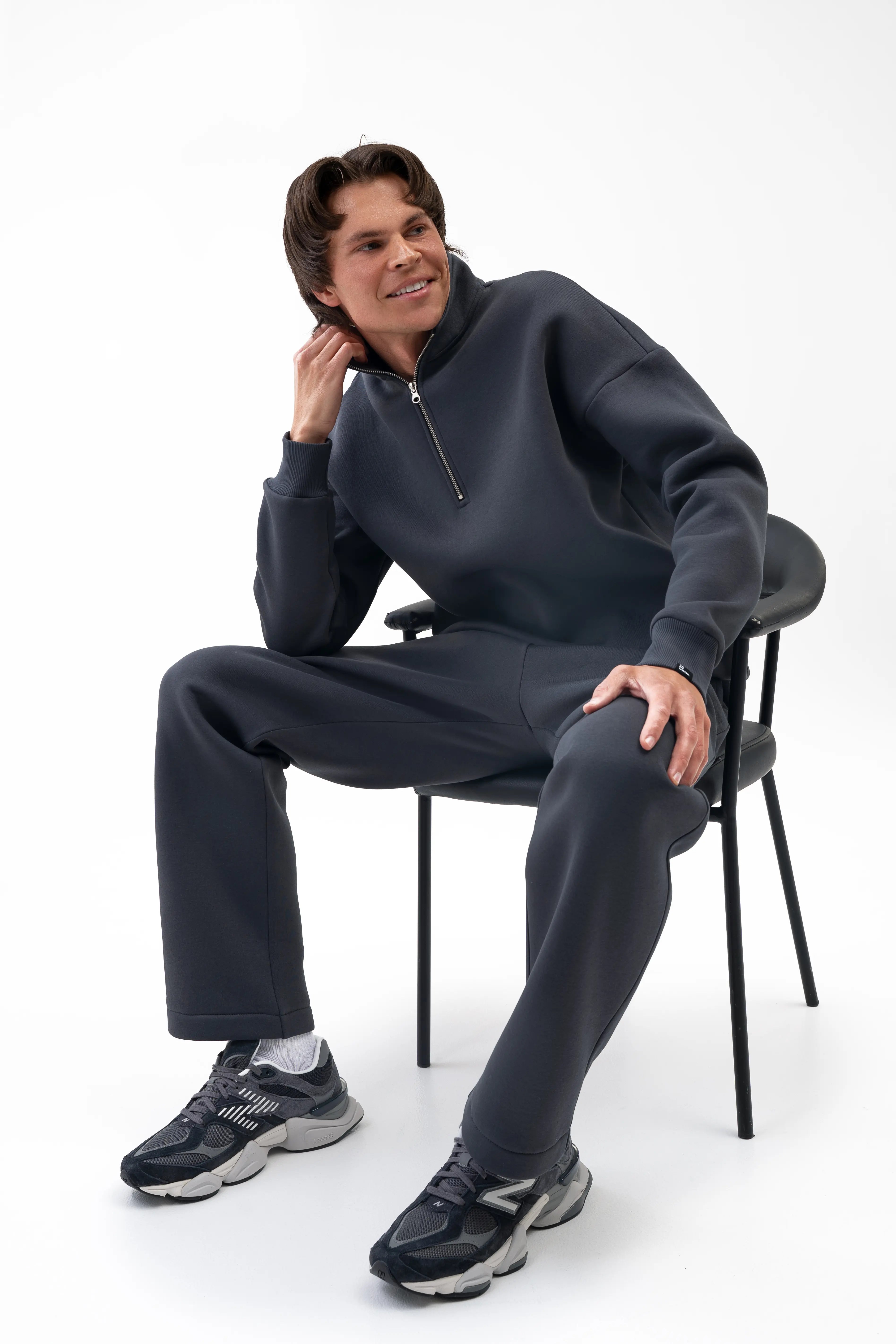 Men’s iron-colour set with a high collar and straight-leg trousers, the model is sitting on a chair