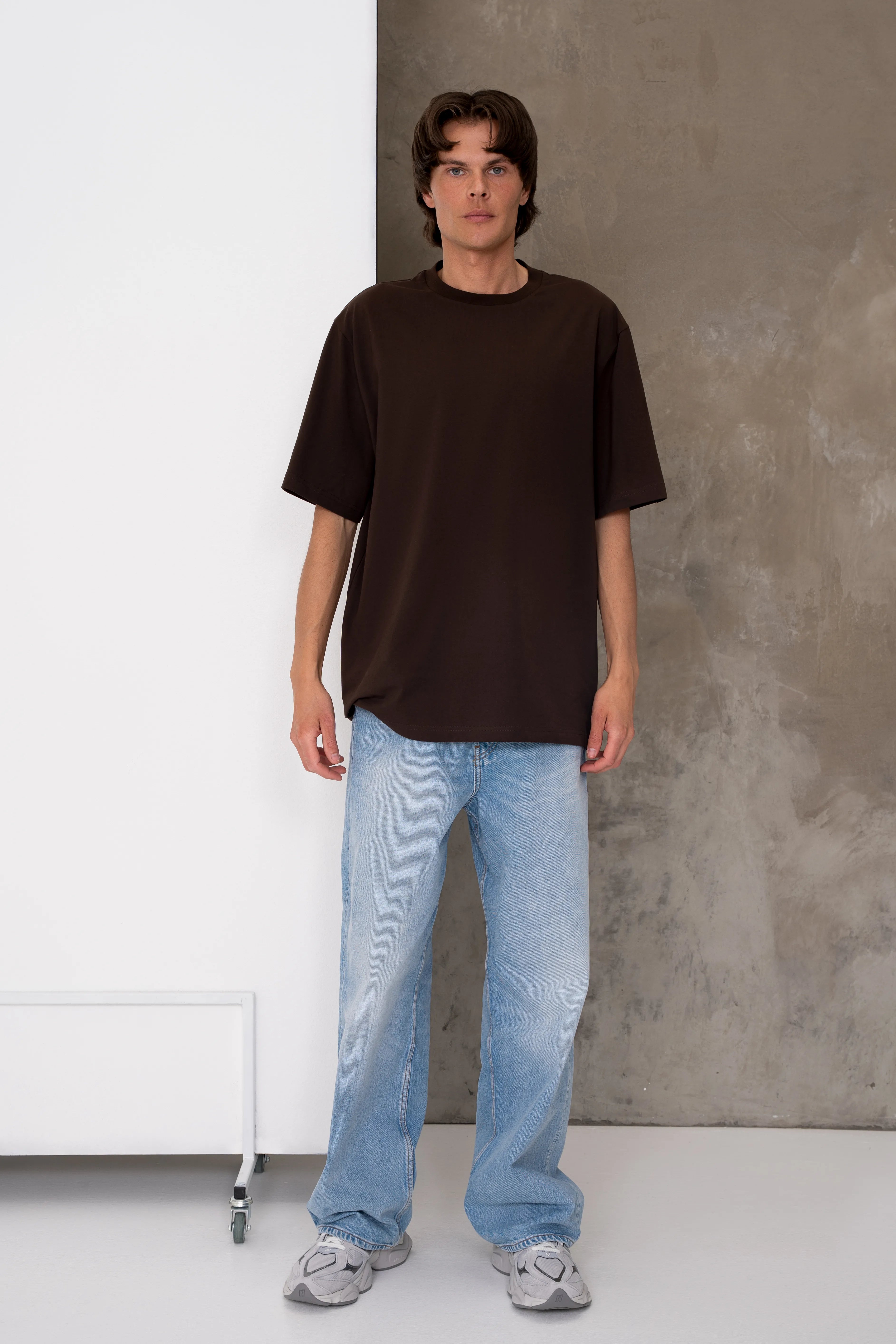 Rudos spalvos vyriški oversized marškinėliai trumpomis rankovėmis su apvalia kaklo iškirpte, nuleista pečių linija ir laisvu siluetu, derinami su šviesiais džinsais, pilnas vaizdas