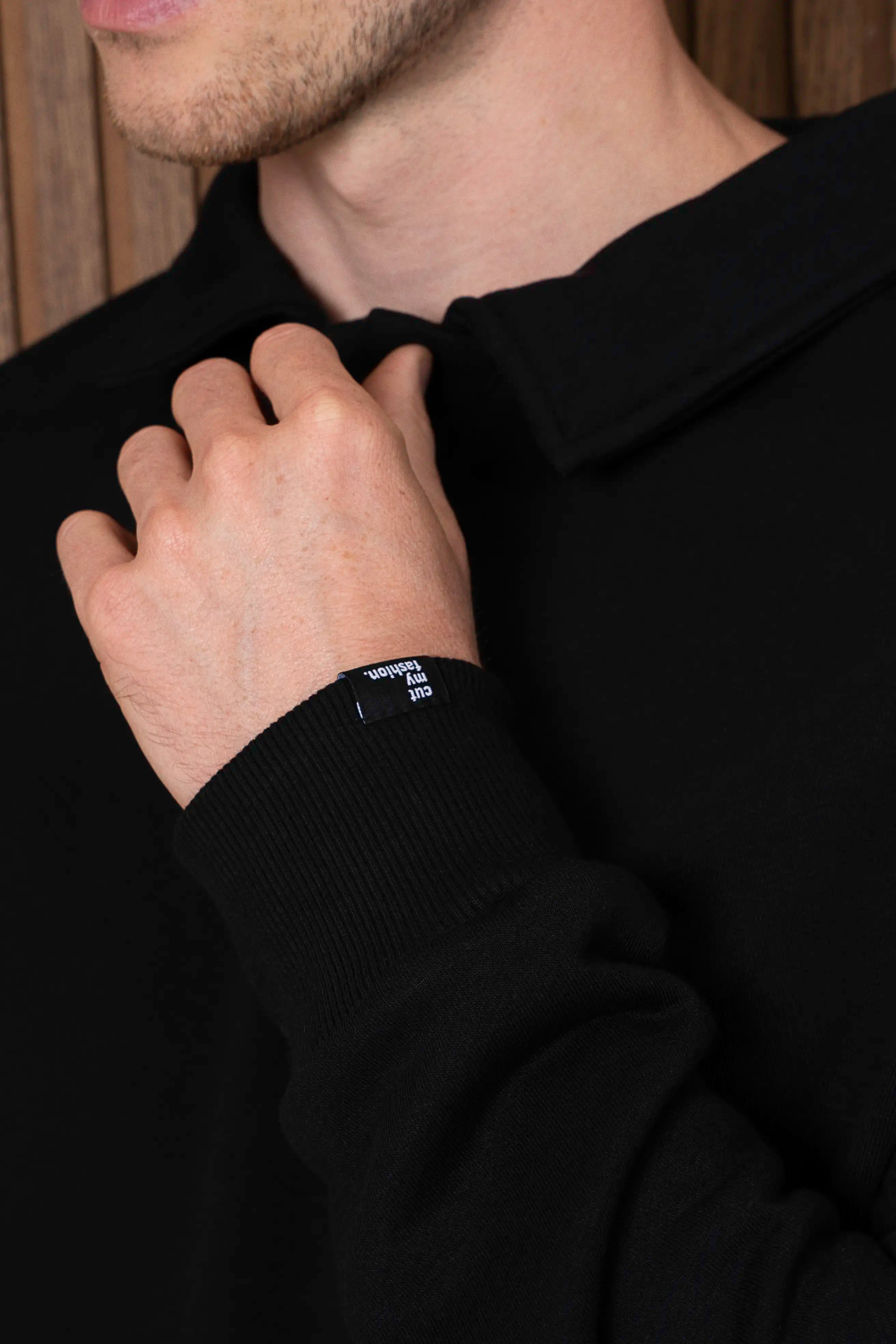 Juodo vyriško džemperio iš audinio be pūkelio detalė, matoma polo tipo apykaklė ir rankogalis su cutmyfashion etikete.